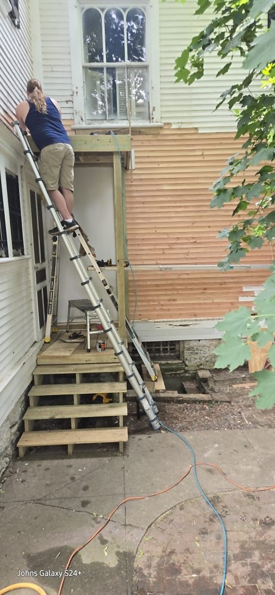 Craftsman on a ladder completing exterior wall repairs on a home