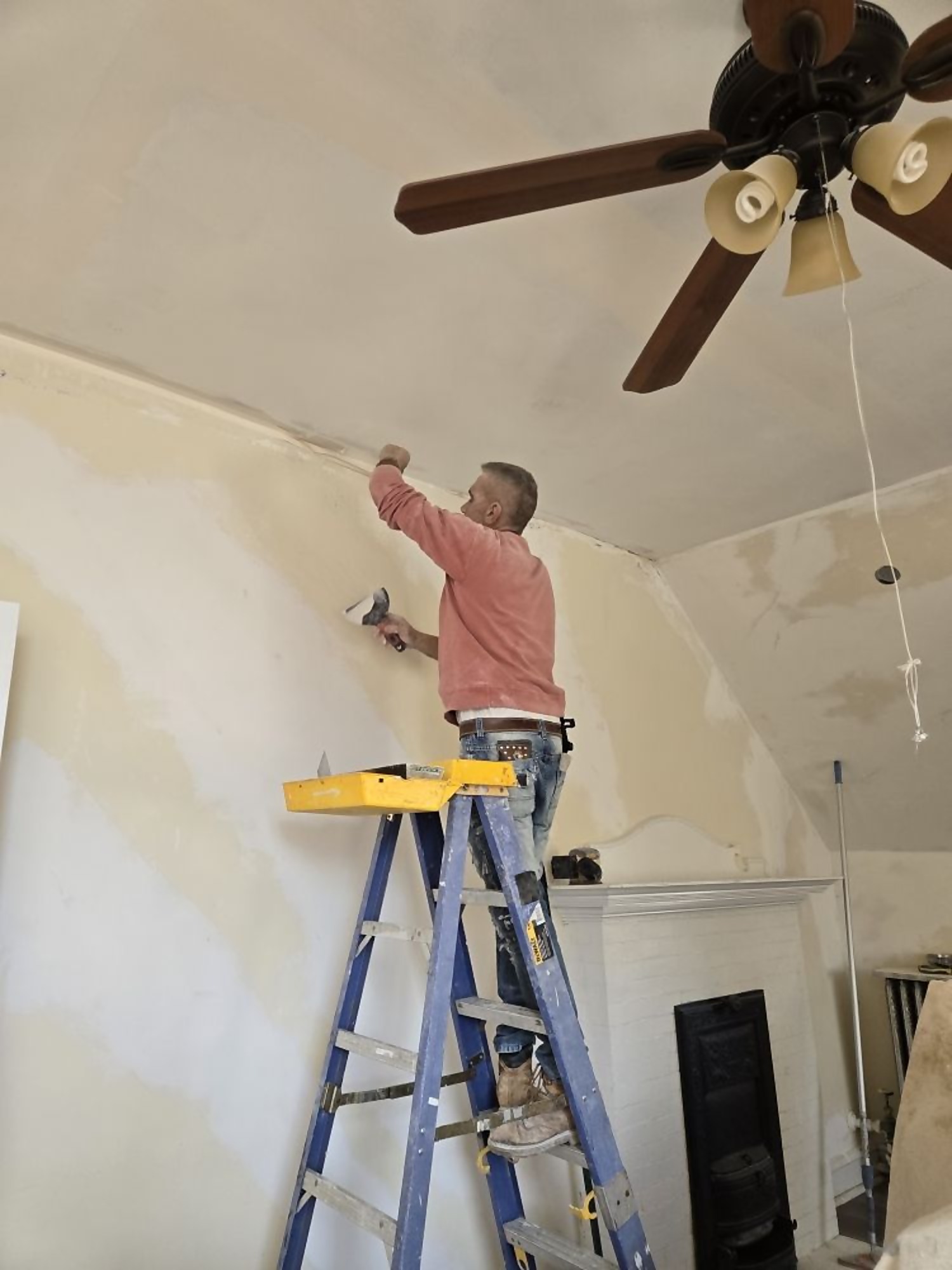Pro One painter on a ladder coating an interior ceiling and wall